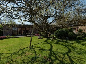 Un bâtiment en briques, avec un grand arbre au premier plan, une pelouse bien entretenue et un mur de pierre en arrière-plan.
