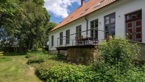 A two-story house with a balcony, surrounded by lush greenery and a well-maintained garden. - Ferienwohnung in Steffenshagen mit Terrasse (Steffenshagen)