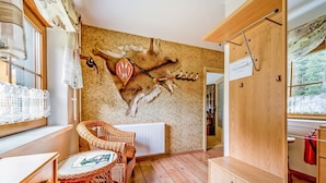 A room with a wooden floor, a wicker chair, a table with a magazine, a wall with a deer mural, and a radiator. - Holiday Home in Jagersgrun With Sauna (Muldenhammer)