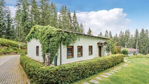 A small, single-story house with a light-colored exterior, surrounded by a well-maintained hedge and a stone pathway leading to the entrance. - Holiday Home in Jagersgrun With Sauna (Muldenhammer)