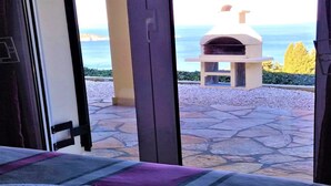 A stone patio with a pizza oven, a view of the sea, and a bed with a purple blanket. - Comfy Apartment in Vinkuran With the Beach Nearby (Corfu)