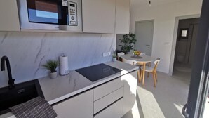 A modern kitchen with a built-in microwave, a sink, and a stove. There is a dining area with a table and chairs, and a potted plant. - Lovely Holiday Home in Pakoštane With Swimming Pool (Pakostane)