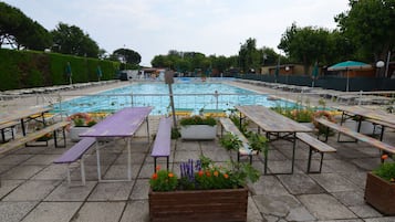 A swimming pool with surrounding picnic tables and benches, surrounded by greenery and trees.