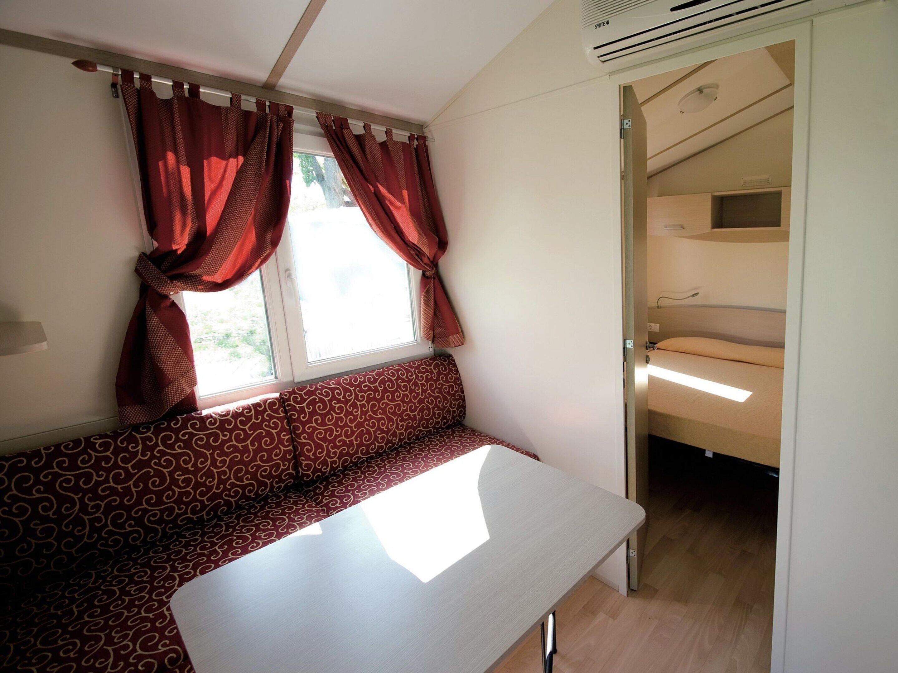 A room with a bed, a bench, a table, and a window with curtains.