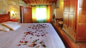 A bedroom with a stone wall, wooden ceiling beams, a bed with rose petals, a wooden wardrobe, and a green curtain. - Rustic Villa with Private Pool near Montepulciano (Montepulciano)