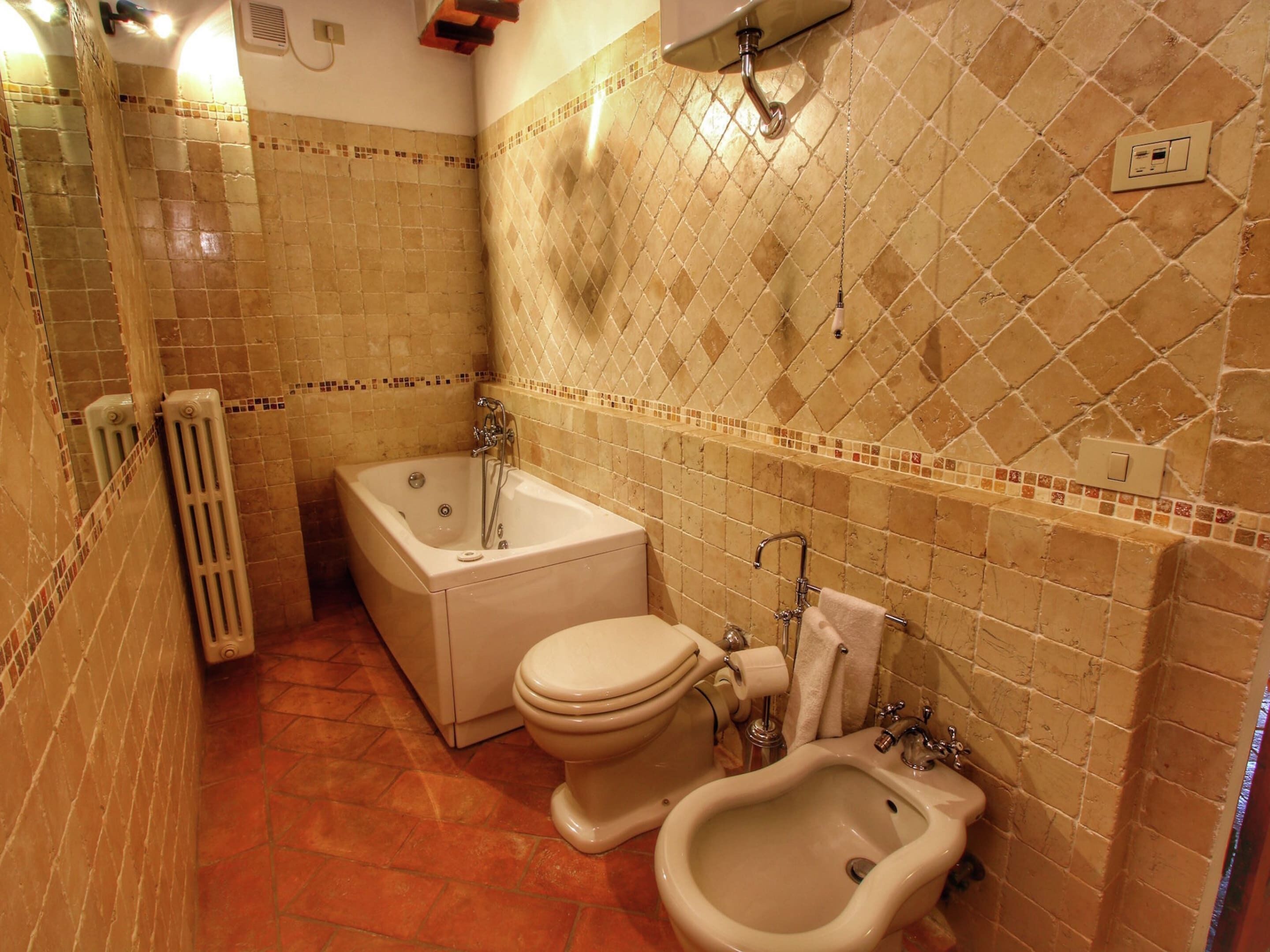 Een badkamer met een badkuip, toilet, bidet en een betegelde wand.