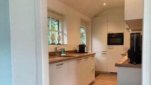 A modern kitchen with white cabinets, a wooden countertop, a sink, a coffee maker, and a microwave. - Beautiful Holiday Home Zeeroos in Zeeland (Koudekerke)