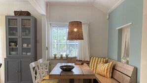 A dining area with a wooden table, white chairs, a bench with yellow and white striped cushions, a wicker pendant light, and a grey cabinet with glass doors. - Beautiful Holiday Home Zeeroos in Zeeland (Koudekerke)