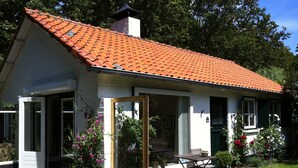 A small house with a tiled roof, a glass door, and a patio with a table and chairs. - Beautiful Holiday Home Zeeroos in Zeeland (Koudekerke)