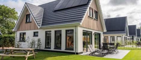 A modern house with a sloped roof, large windows, and a patio area with outdoor furniture.