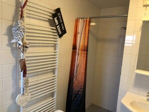 A bathroom with a white tiled wall, a white radiator, a shower curtain, and a sink with a mirror.