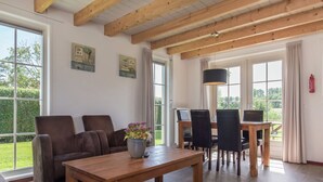 A spacious living area with a wooden coffee table, a sofa, and a dining table with chairs. There are large windows providing natural light and views of the outdoors. - Atmospheric Holiday Home Near the Oosterschelde (Wemeldinge)