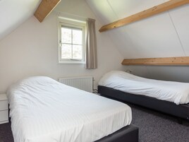 Un dormitorio con dos camas, una ventana con cortinas, un radiador y vigas de madera.