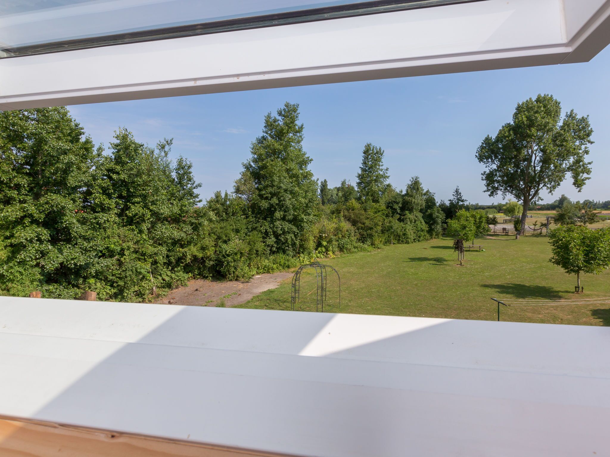 A view from a window overlooking a grassy area with trees and a clear sky.