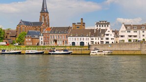Een historische stad met een opvallende kerk en een hoge kerktoren, met daaraan een rustige rivier met verschillende boten afgemeerd.