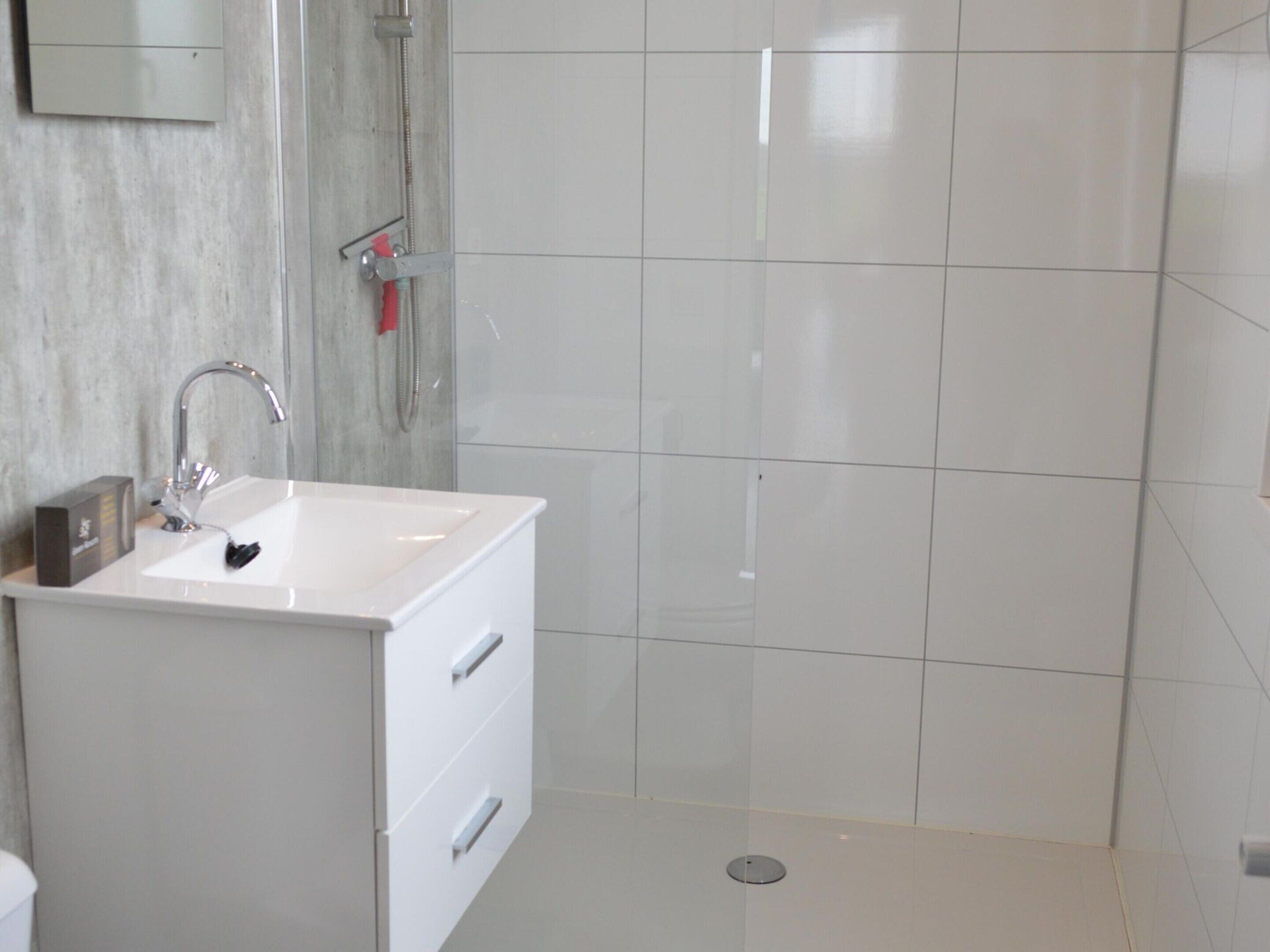 A modern bathroom with a white sink, a shower, and a tiled wall.