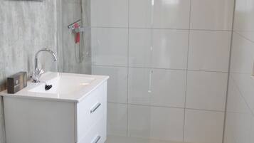 A modern bathroom with a white sink, a shower, and a tiled wall.