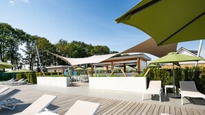 Een moderne buitenlounge met witte ligstoelen en een overdekte zithoek met parasols.