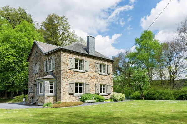 A stone house with a chimney, a porch, and a well-maintained lawn.