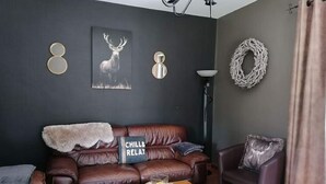 A living room with a brown leather sofa, a coffee table, and a wall-mounted lamp. - Sunny Garden Cottage, Alle (Vresse-sur-Semois)