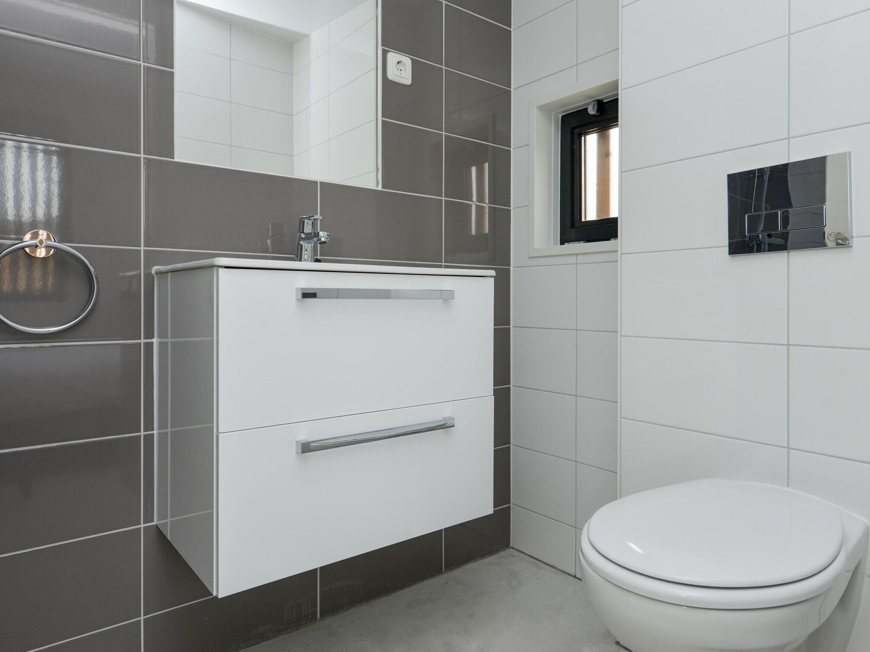 Un baño moderno con lavamanos, espejo y retrete blancos.