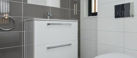 Un baño moderno con lavamanos, espejo y retrete blancos.