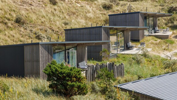 Eine moderne, mehrstöckige Holzhütte mit einer Terrasse und Sitzbereich im Freien, umgeben von einer natürlichen Landschaft.