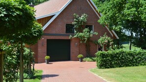 A brick house with a large garage door, surrounded by greenery and trees. - Ferienhaus in Lindern mit Garten & Terrasse (Lindern)