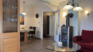 A modern living room with a glass coffee table, a red sofa, a fireplace, and a dining area with chairs and a table. - Ferienhaus in Lindern mit Garten & Terrasse (Lindern)