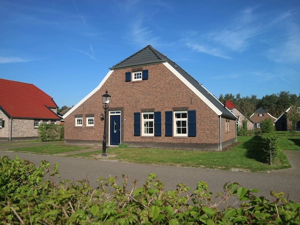 A brick building with a steeply pitched roof, a central door, and windows with shutters.