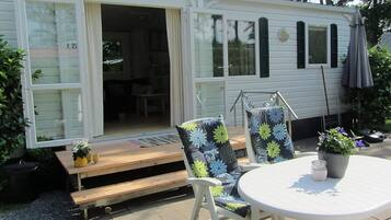 A mobile home with a patio area featuring a table, chairs, and a potted plant.