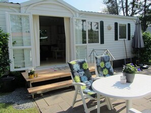 A mobile home with a patio area featuring a table, chairs, and a potted plant. - Captivating Chalet with Microwave near Wadden Sea (Tzummarum)