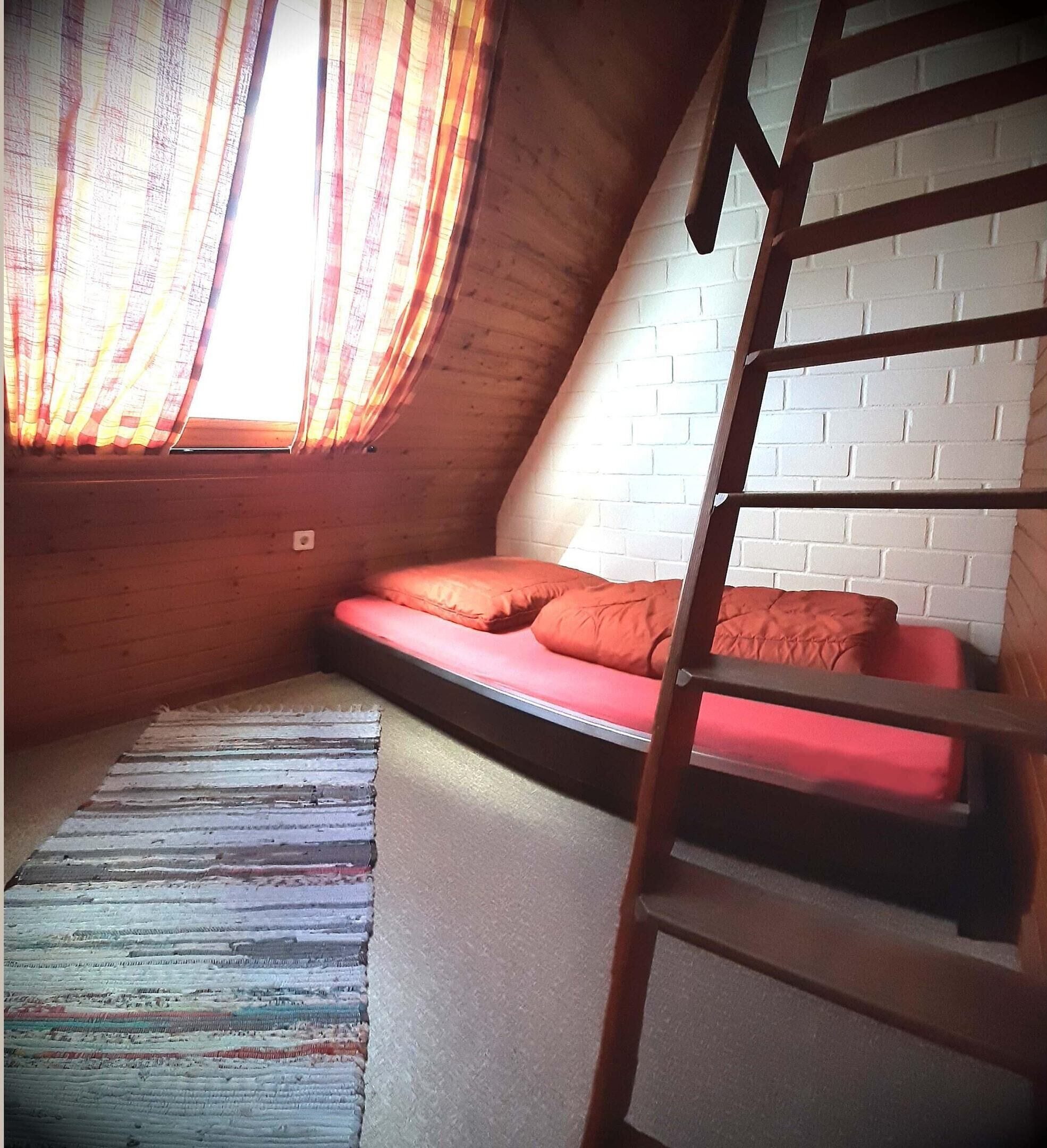 Ein Schlafzimmer im Loft-Stil mit schrägverdeckter Decke, einer Holzleiter und einem roten Sofa, sowie einem gestreiften Teppich.