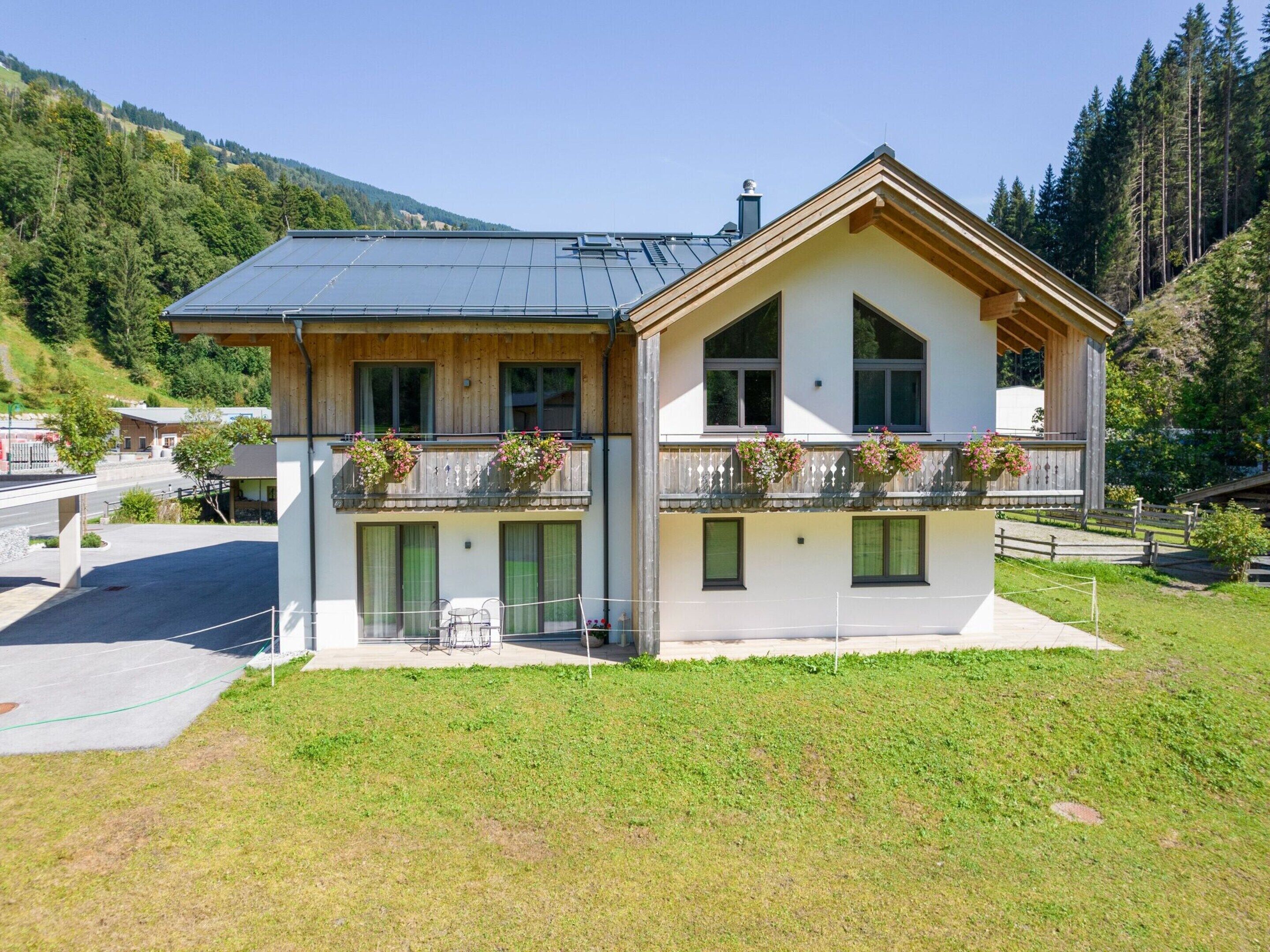 Eine zweistöckige Chalet mit einem geneigten Dach, Holzbalkonen mit Blumenkästen und Blick auf eine Berglandschaft.