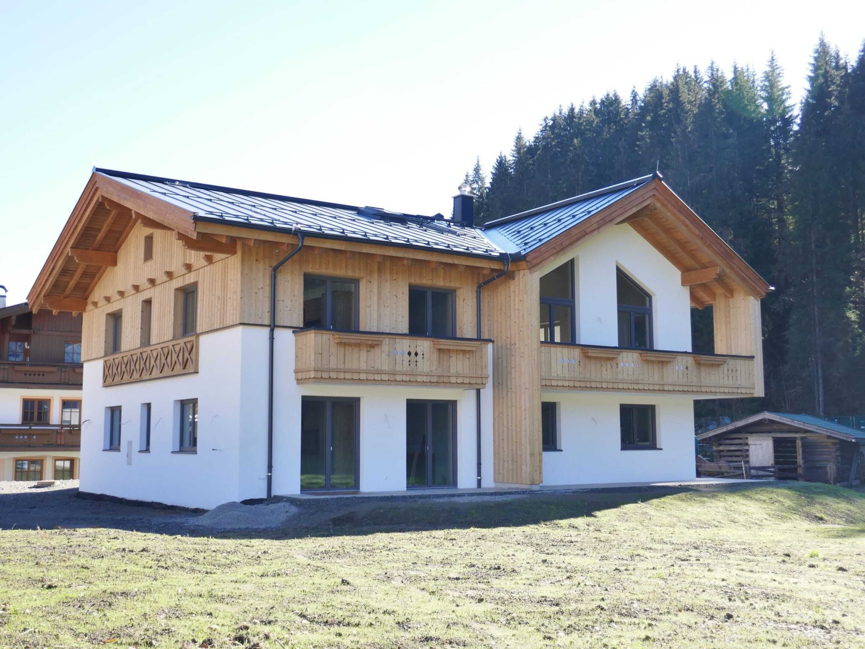 A two-story wooden chalet with a sloped roof, large windows, and a balcony.