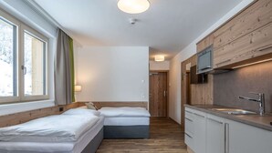 A modern, compact hotel room with two beds, a kitchenette, and a view of a snowy landscape through large windows. - Chalet in Saalbach Near Ski Lift and Sauna (Saalbach-Hinterglemm)