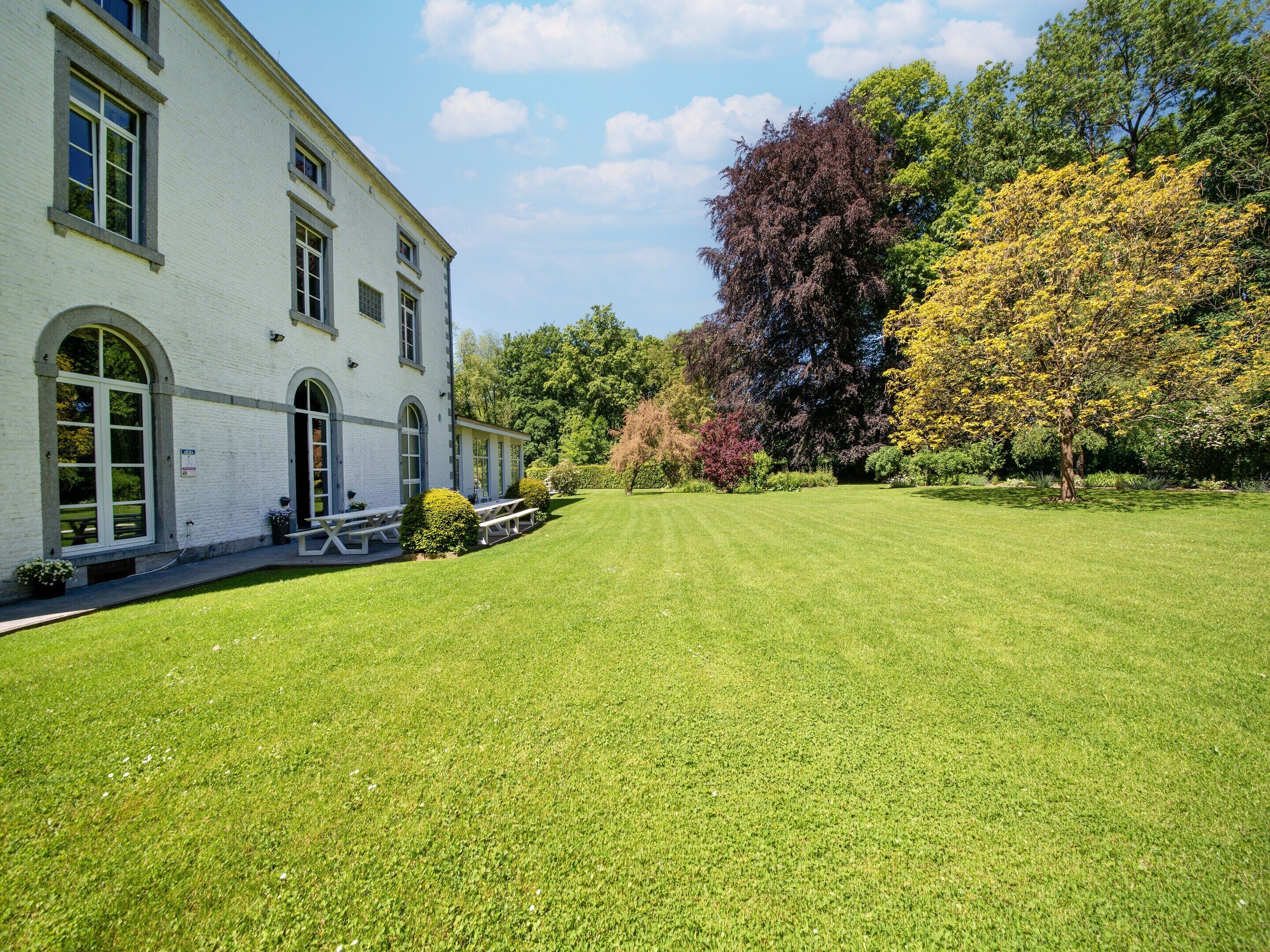 A white building with arched windows, a lawn, and trees with autumn foliage.