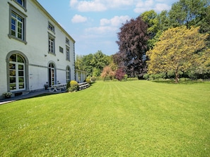 A white building with arched windows, a lawn, and trees with autumn foliage.