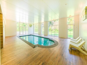 Una piscina con cubierta de madera, ventanas amplias y vistas a zonas verdes.