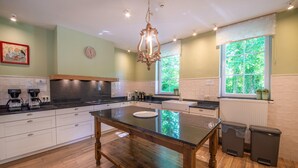 A kitchen with a central island, wooden cabinets, a chandelier, and a window with a view of greenery. - Luxurious Mettet Mansion (Mettet)