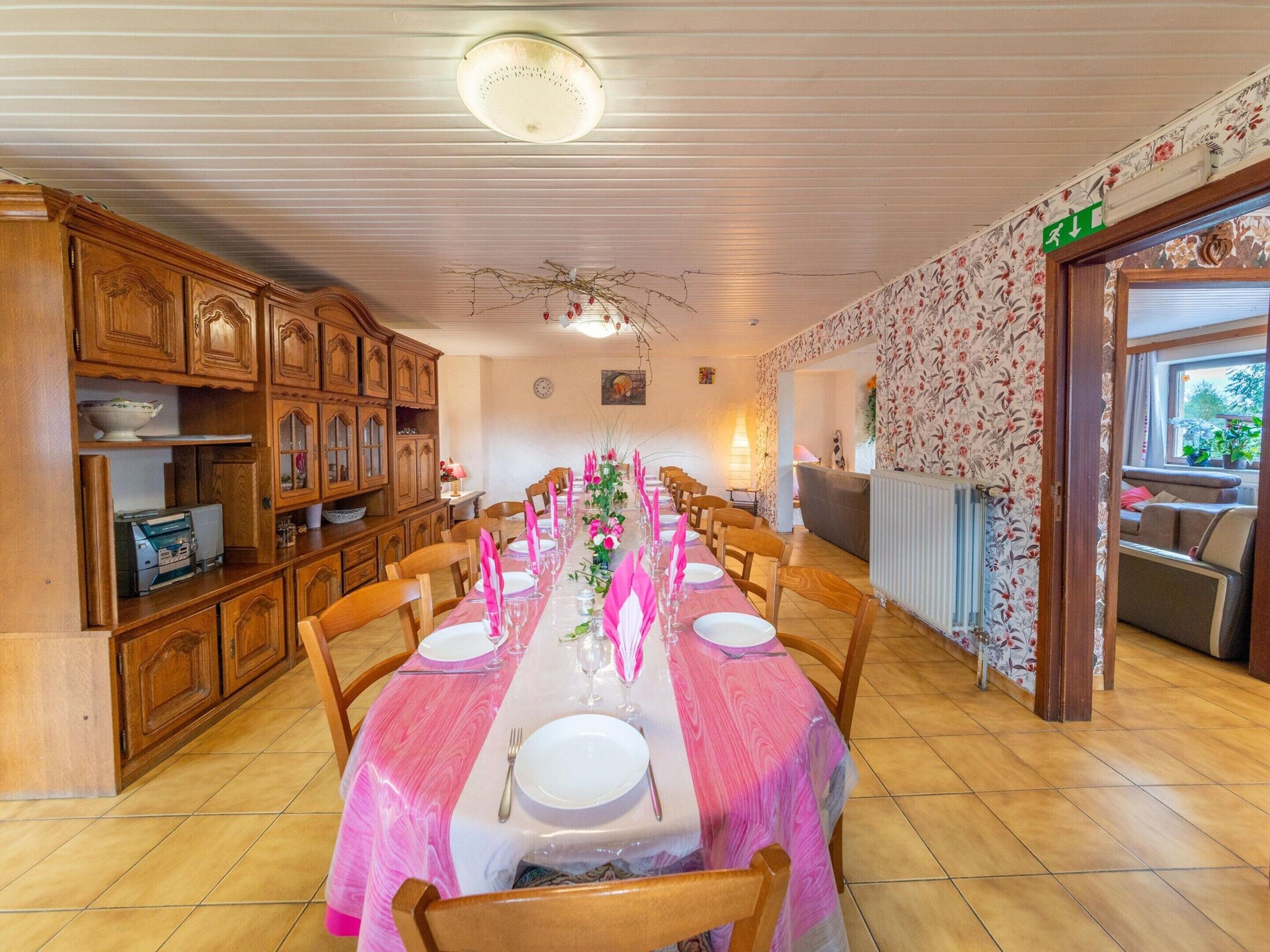 Un comedor con una mesa larga dispuesta para una comida, armarios de madera y una pared cubierta de papel tapiz floral.