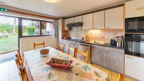 A modern kitchen with a dining area, featuring a large window, wooden cabinets, and a stainless steel oven. - Holiday Home in Montleban With Garden (Gouvy)