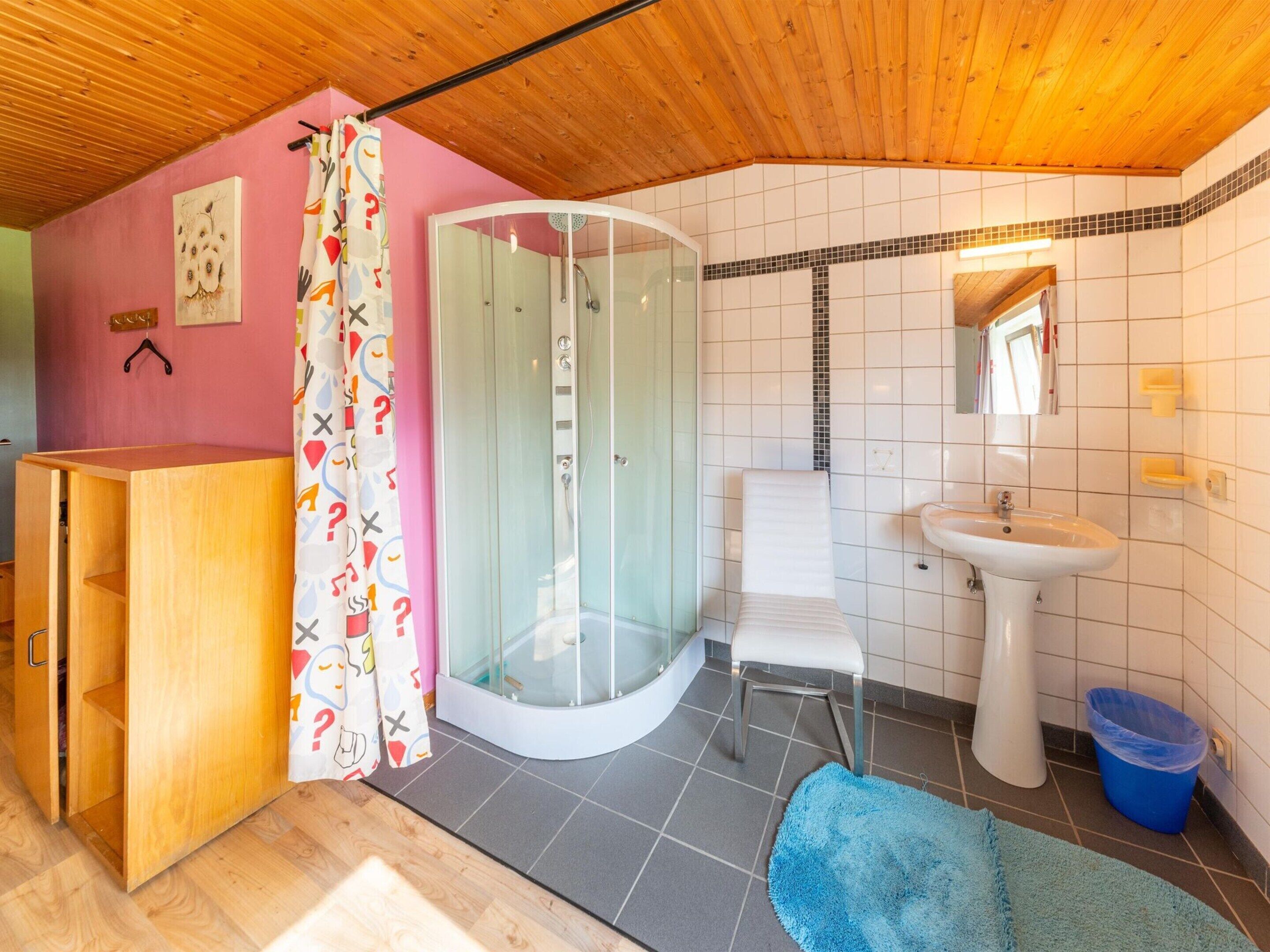 A bathroom with a shower, sink, and a wooden cabinet.