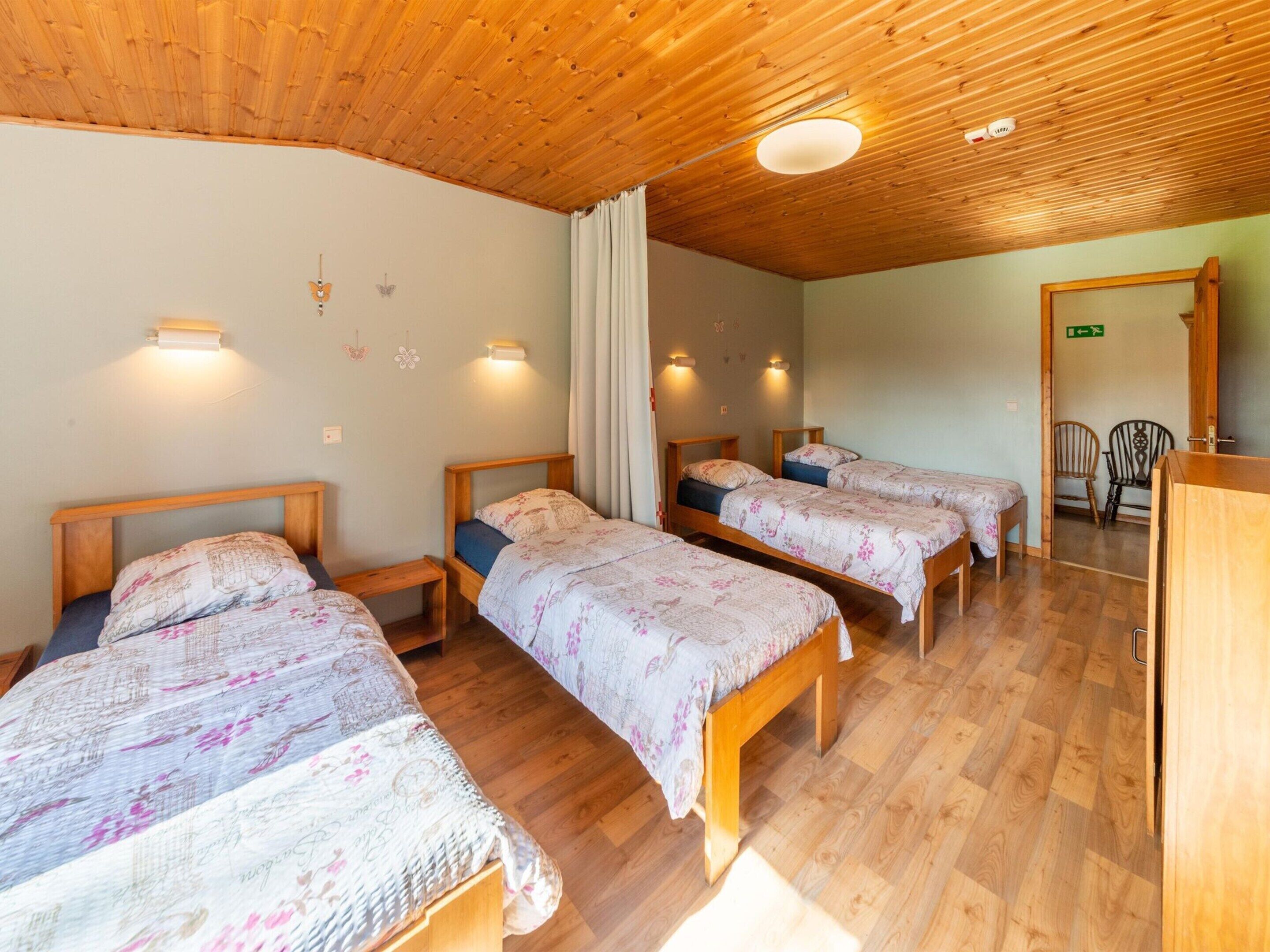 A room with three wooden beds, each with a floral-patterned bedspread, wooden headboards, and bedside tables.