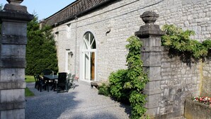 Un edificio de piedra con un camino de grava que conduce a una puerta. Hay mesas y sillas al aire libre.