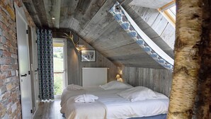 A bedroom with a sloped ceiling, exposed wooden beams, a brick wall, and a large window. - Comfortable Chalet With Indoor Pool, Hammam and Sauna Near Stoumont (Stoumont)