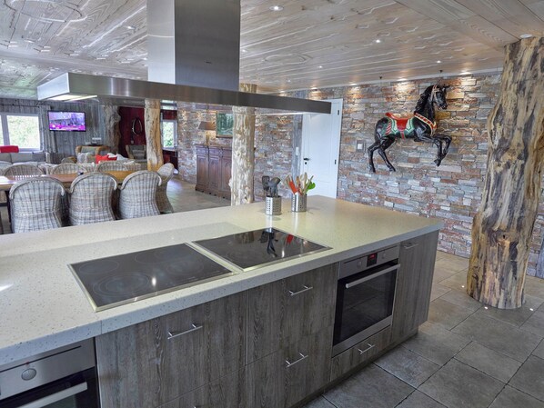A modern kitchen with a large island, built-in appliances, and a rustic stone wall.