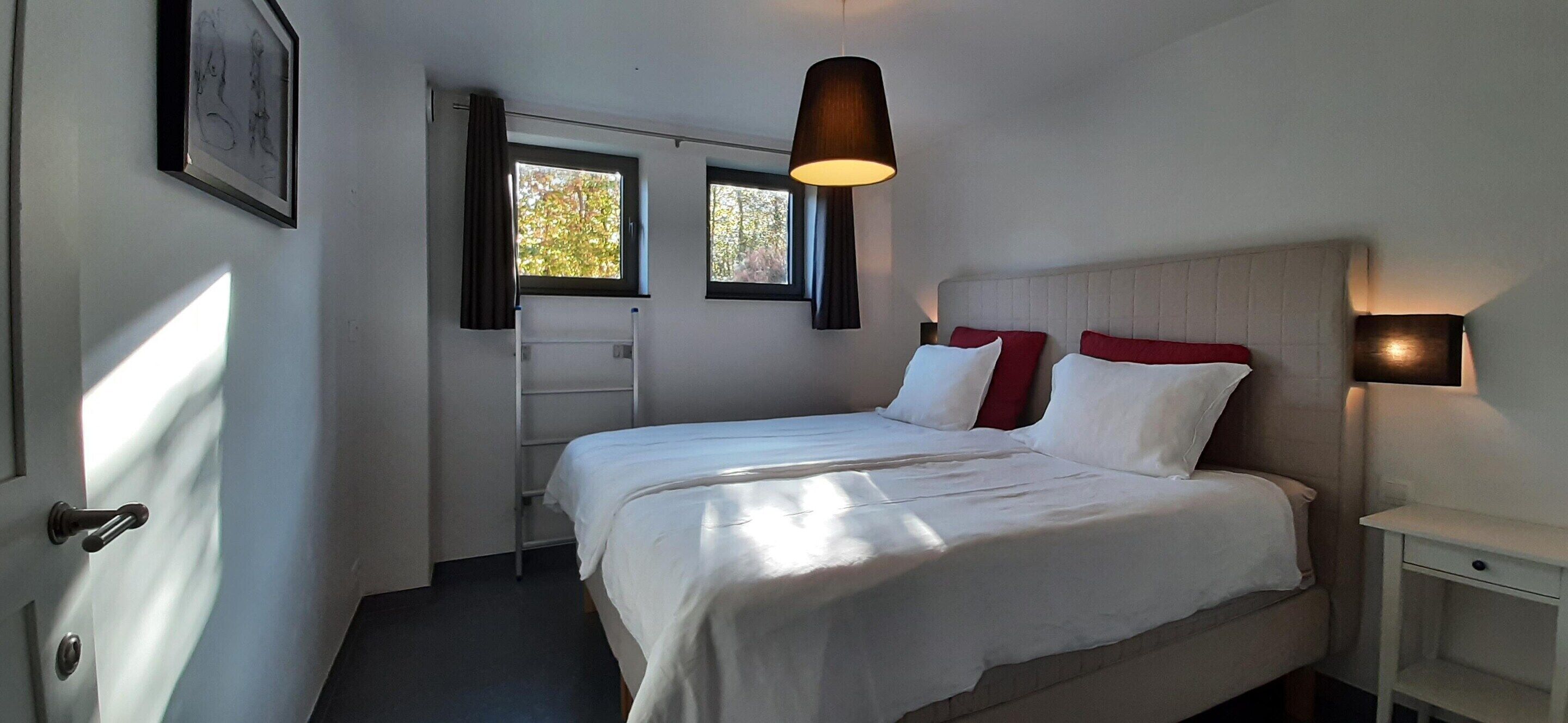 A bedroom with a bed, a window, a ladder, and a nightstand.