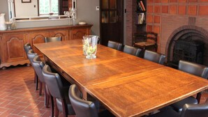 Une salle à manger avec une longue table en bois, des chaises noires, une cheminée et un mur en briques.