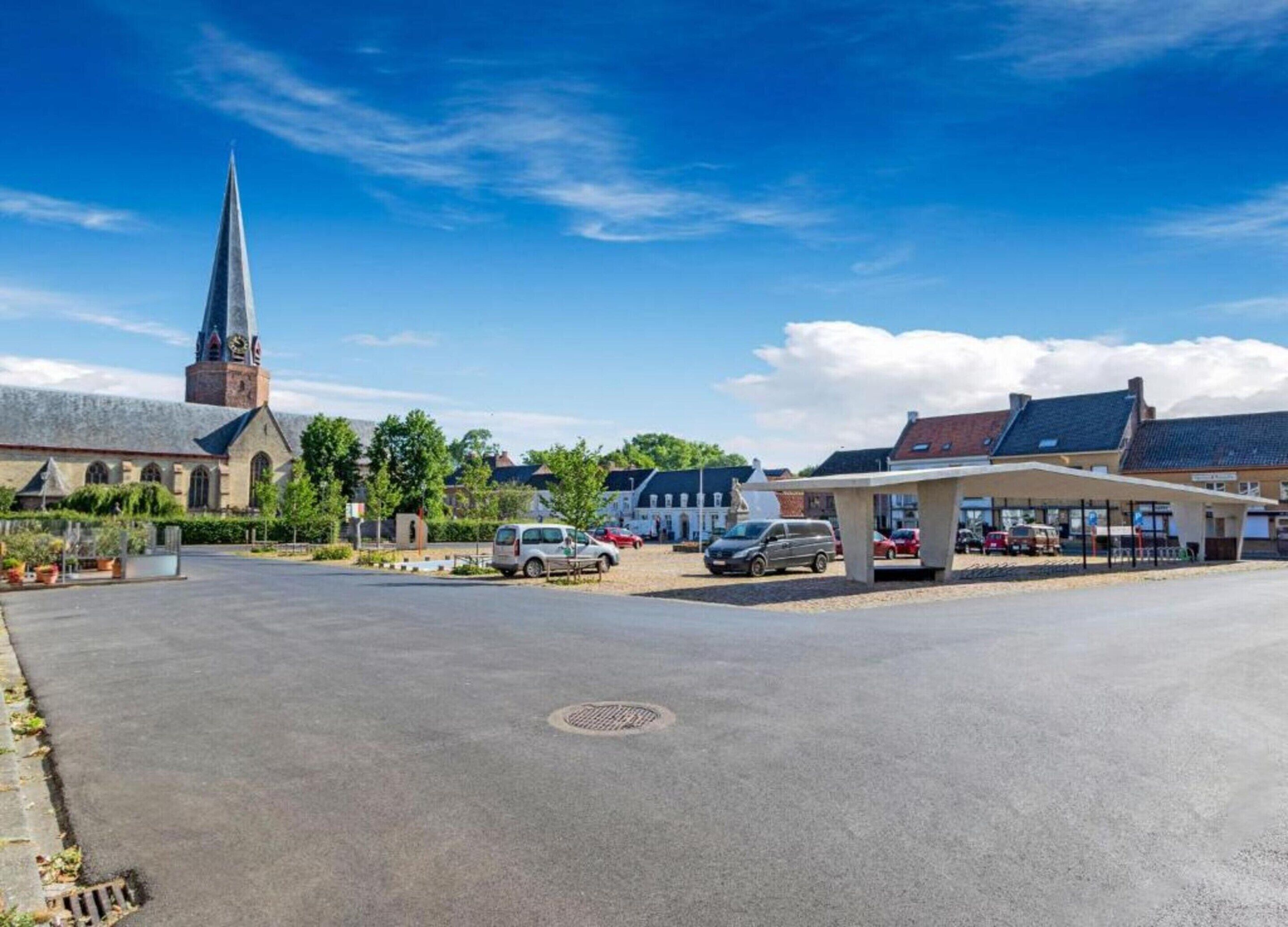 A church with a tall steeple, a parking area with cars, and a covered building with a sign.